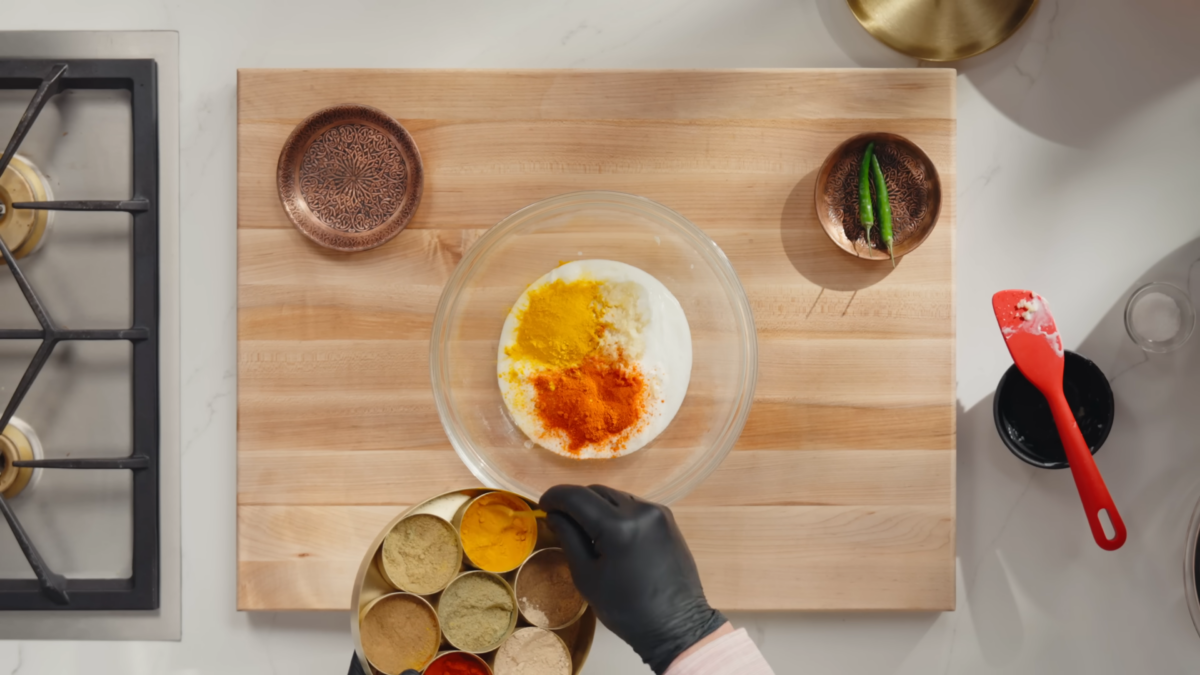 A man adding spices to a mixing bowl with yogurt.