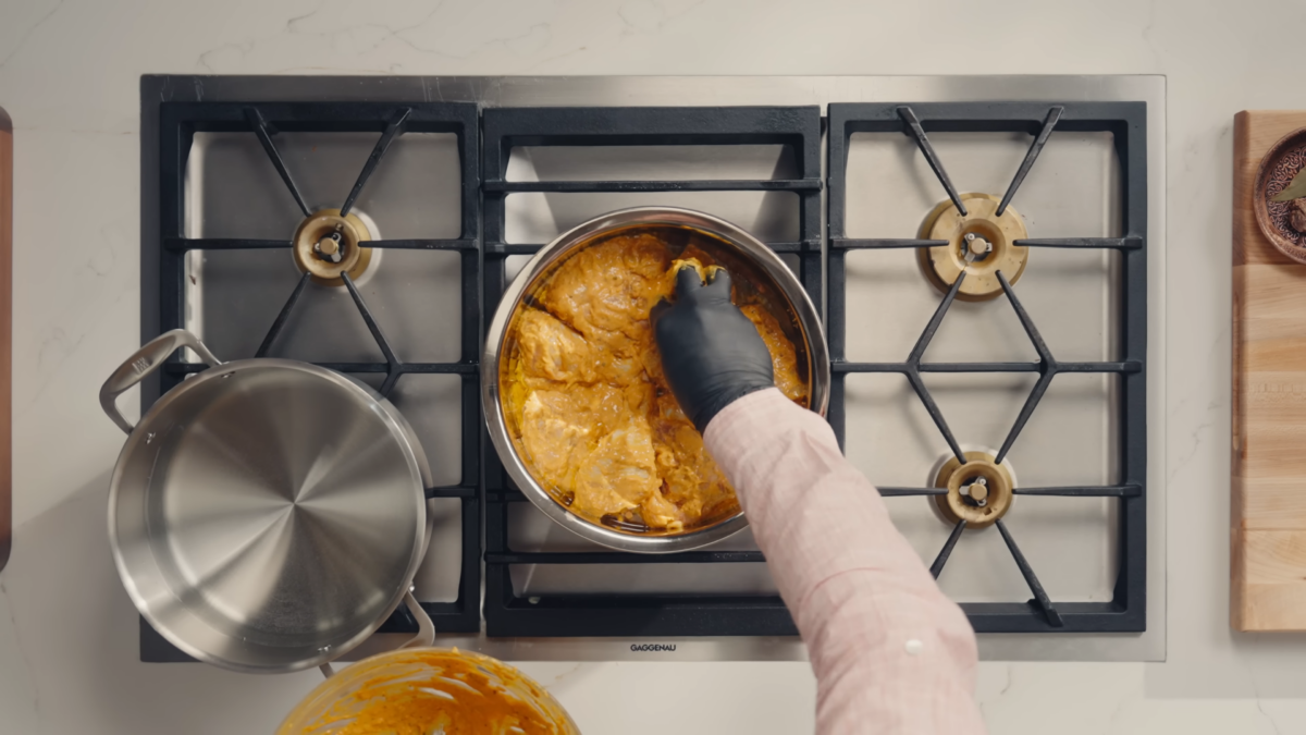 A male chef placing marinaded chicken in a pot.