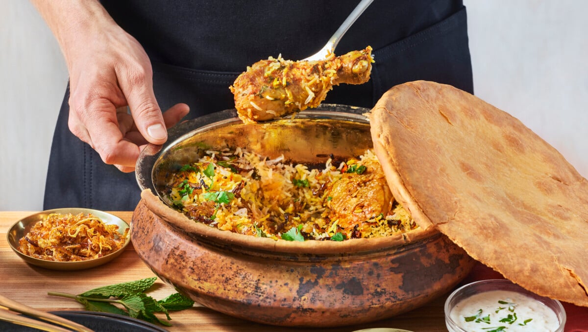 A man scooping chicken biryani out of a metal pot.
