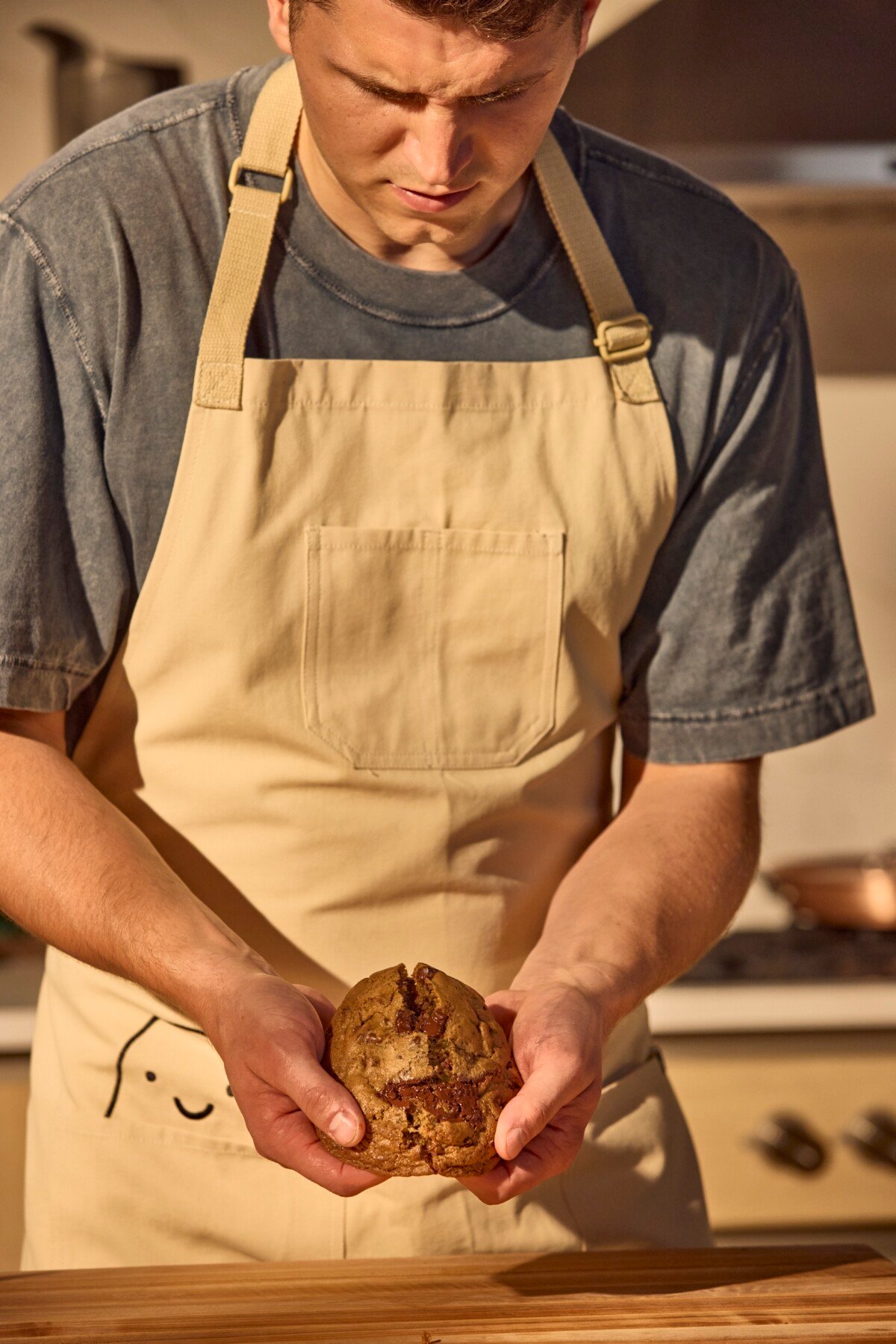A male chef splitting a chocolate chip cookie in half.