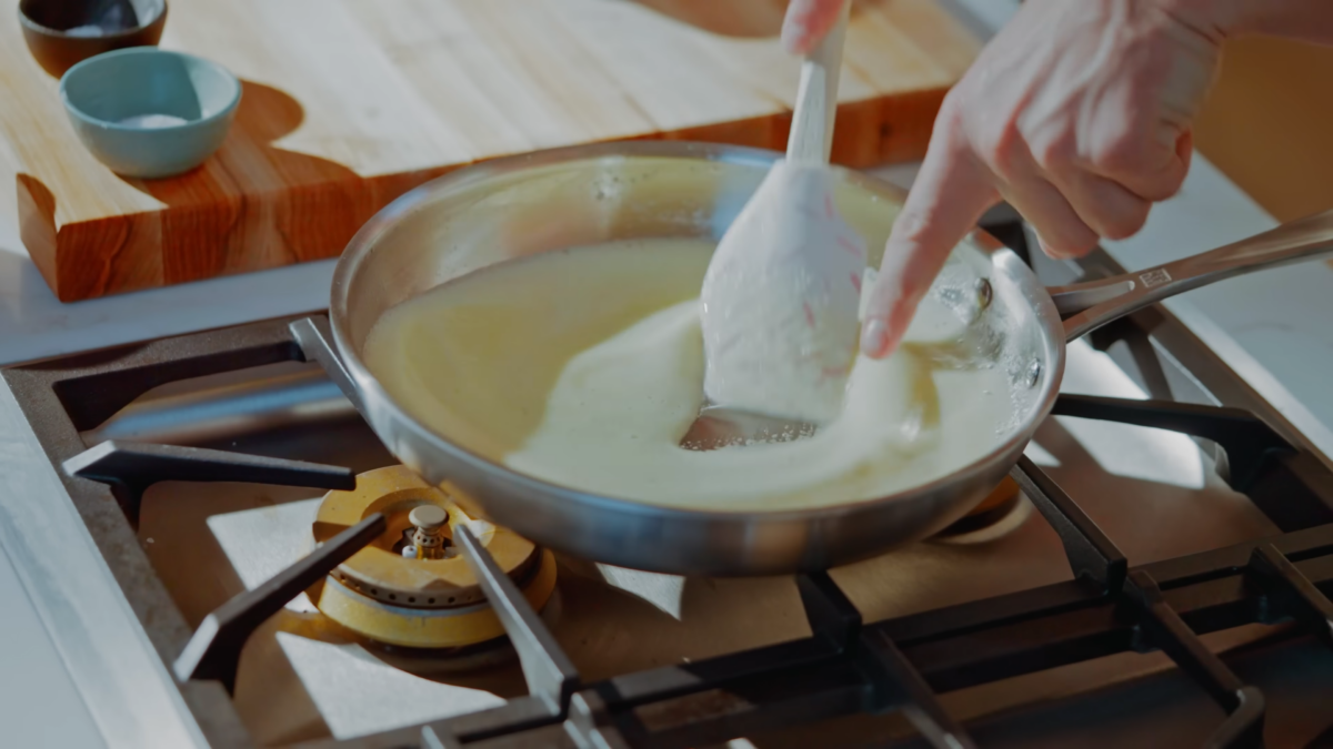 Foamy butter mixed in a stainless steel pan with a rubber spatula.