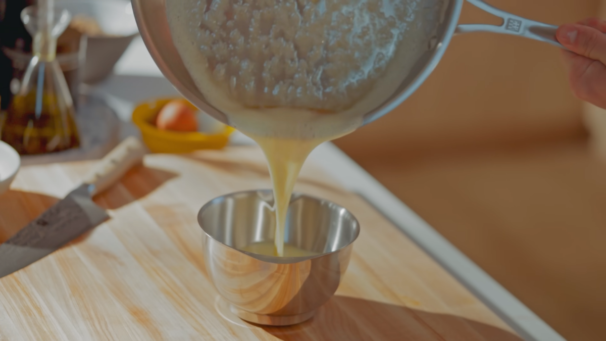 Browned butter being poured into a stainless steel bowl.