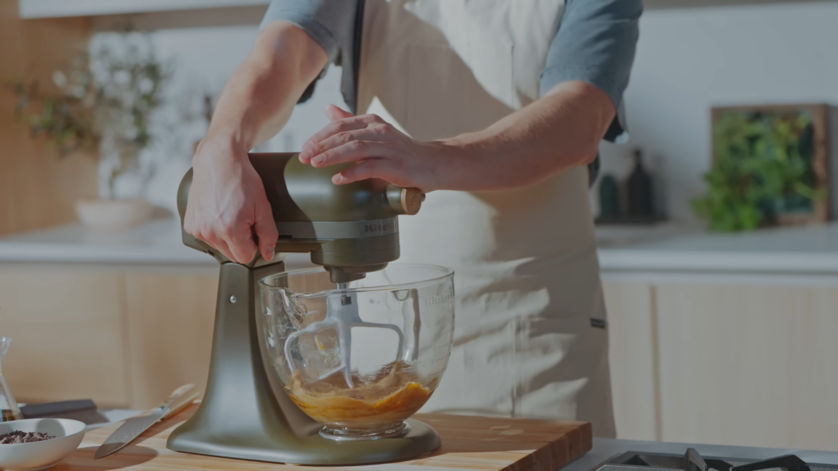 An electric mixer mixing a glass bowl of wet ingredients for chocolate chip cookies.