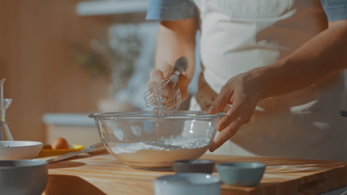 A man whisking flour in a glass bowl.