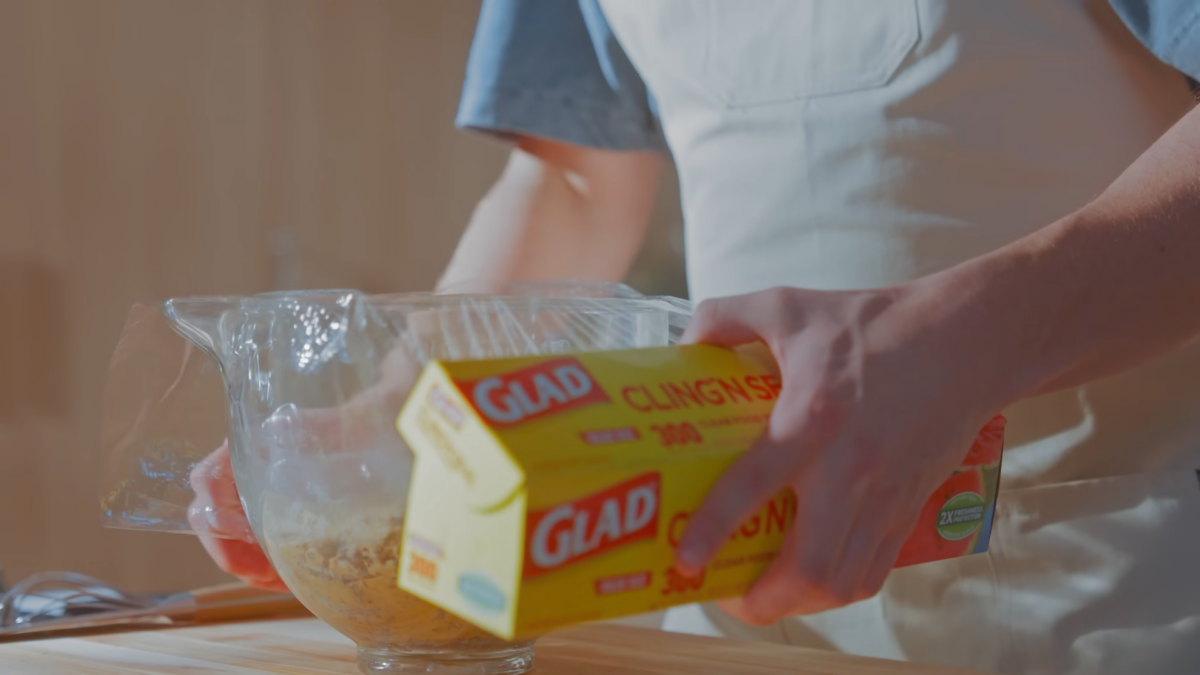 A man covering a bowl of chocolate chip cookie dough with plastic wrap.