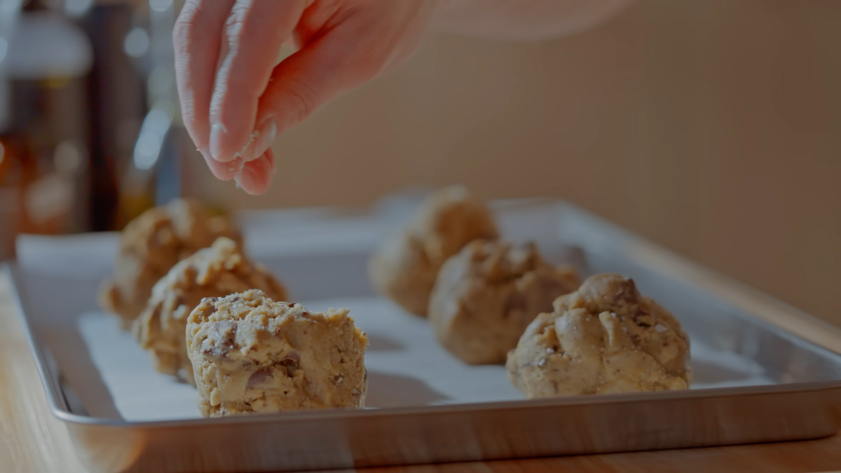 Salt being sprinkled on balls of chocolate chip cookie dough.