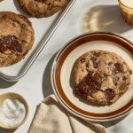 Brown butter chocolate chip cookies on a baking sheet and one on a plate.