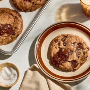 Brown butter chocolate chip cookies on a baking sheet and one on a plate.