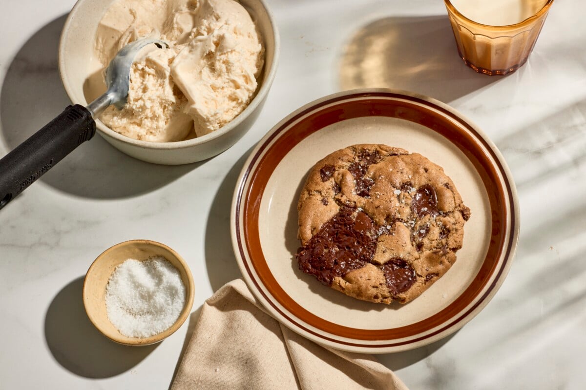 A brown butter chocolate chip cookie on a plate next to a bowl of ice cream.