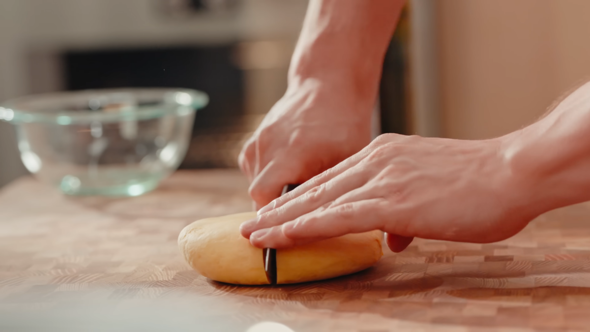 A male chef cutting a ball of dough in half.
