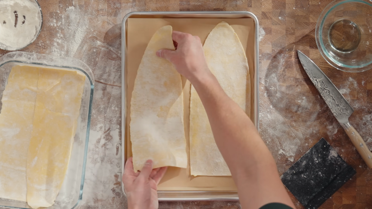 A man placing sheets of homemade lasagna dough on a baking sheet.