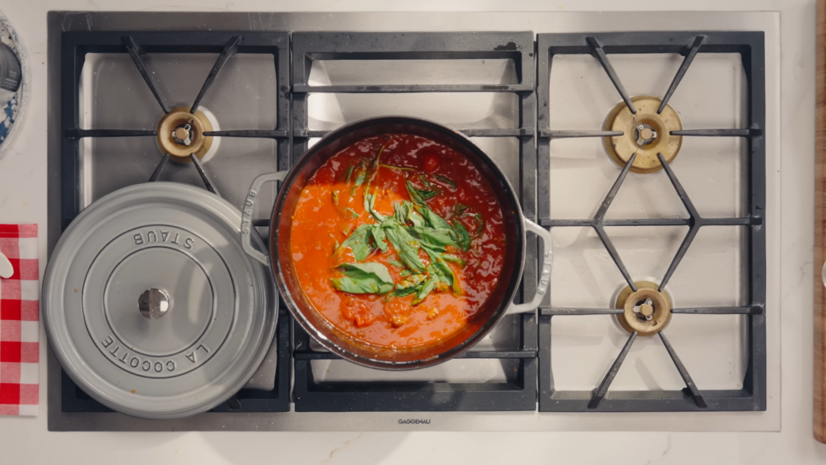 A pot of red lasagna sauce with fresh basil leaves on top.