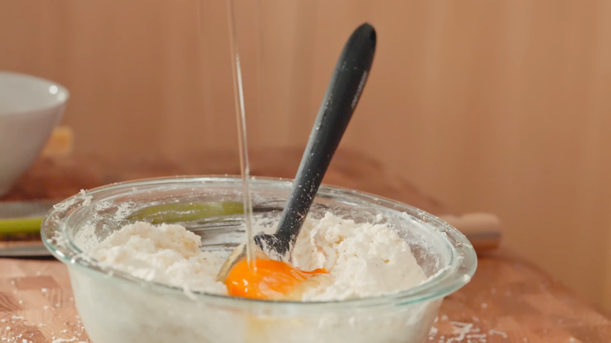 An egg cracked into a glass bowl of ricotta cheese filling.