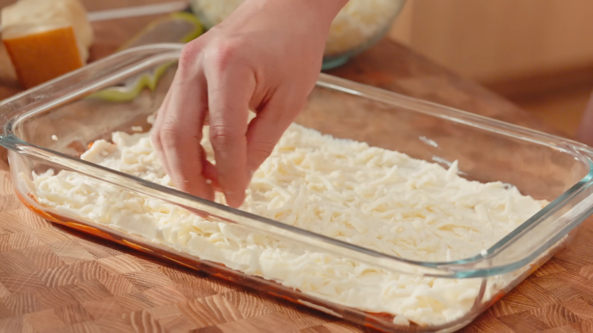 Shredded cheese sprinkled in a glass baking dish.