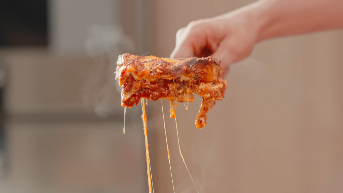 A man holding a slice of gooey stringy homemade lasagna.