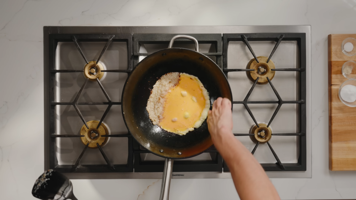 Egg cooking in a wok with minced garlic and onions.