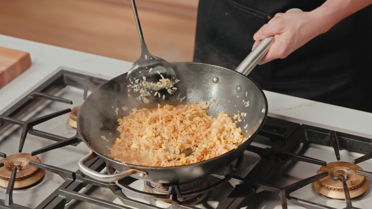A male chef stirring fried rice in a wok.