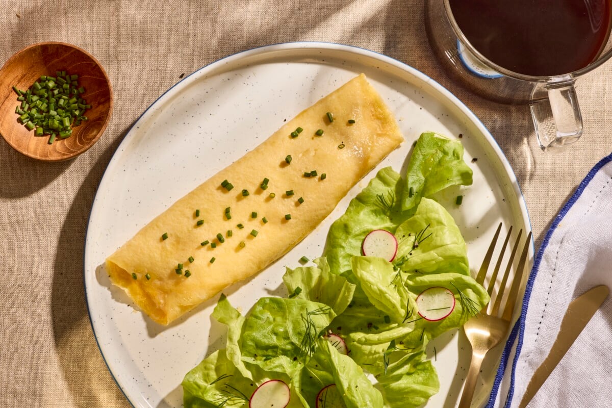 A French omelette on a plate next to a salad.