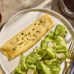 A French omelette on a plate next to a salad.