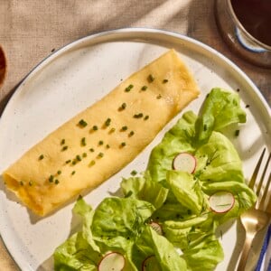 A French omelette on a plate next to a salad.
