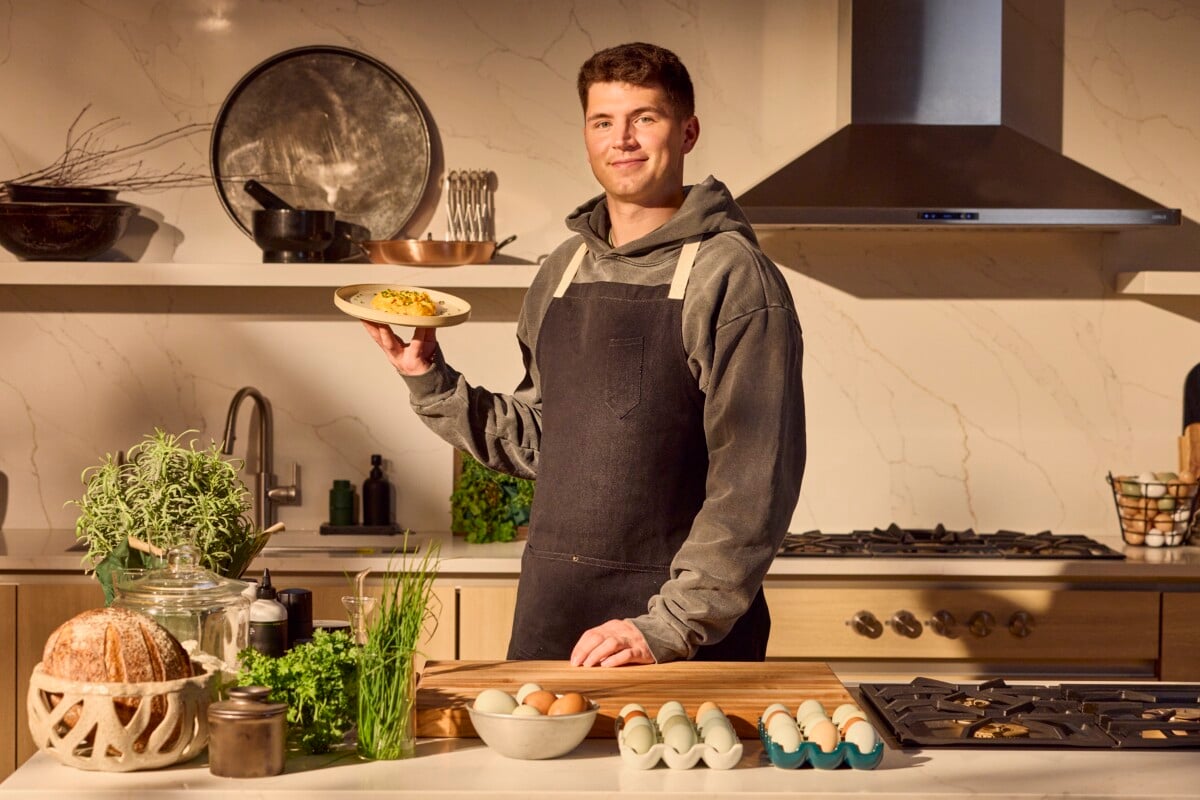 A male chef holding a plate of scrambled eggs.