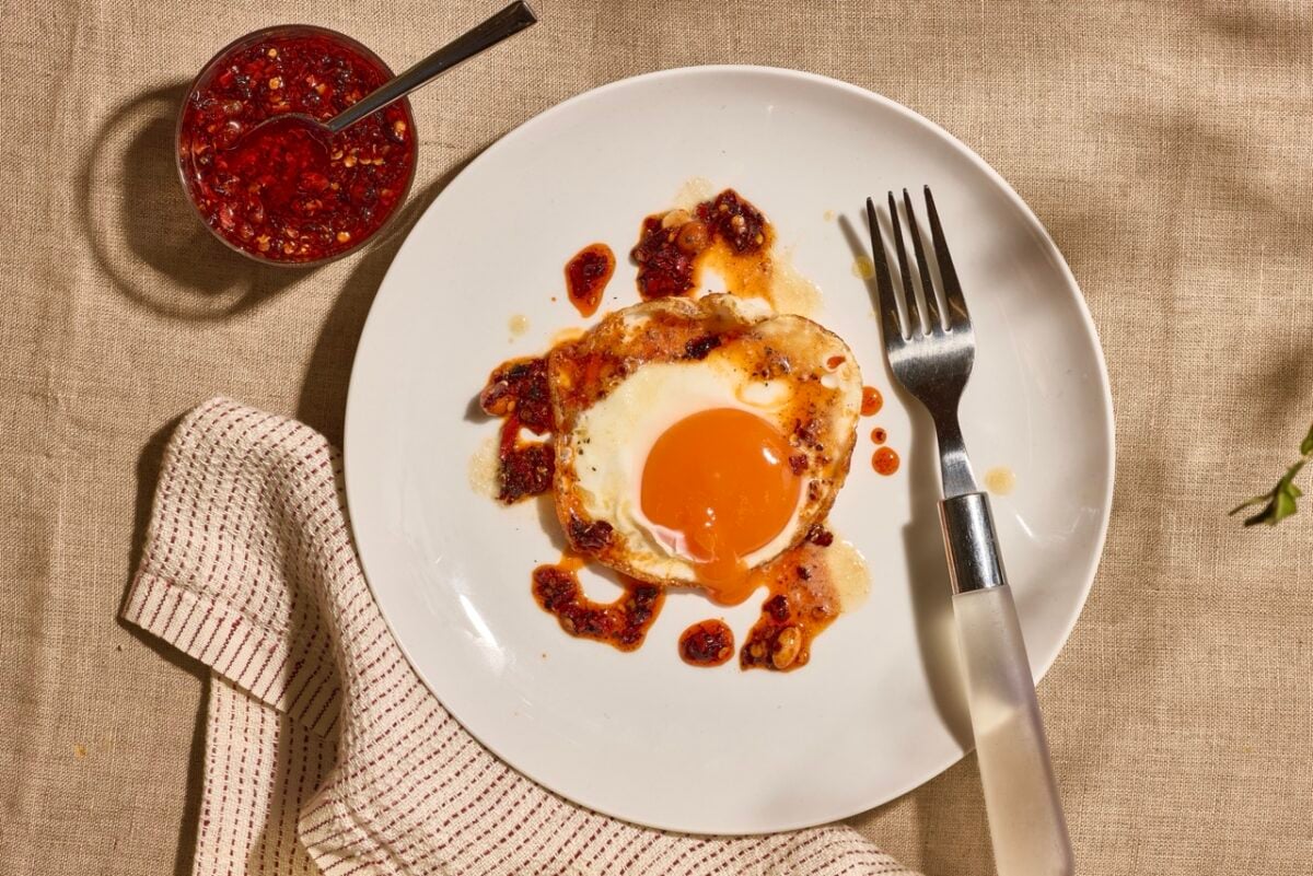 A sunny side up egg on a plate topped with brown butter and chili crisp.