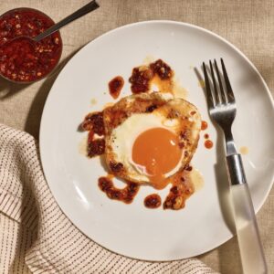 A sunny side up egg on a plate topped with brown butter and chili crisp.