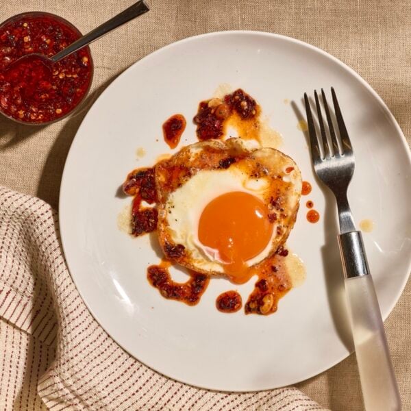 A sunny side up egg on a plate topped with brown butter and chili crisp.