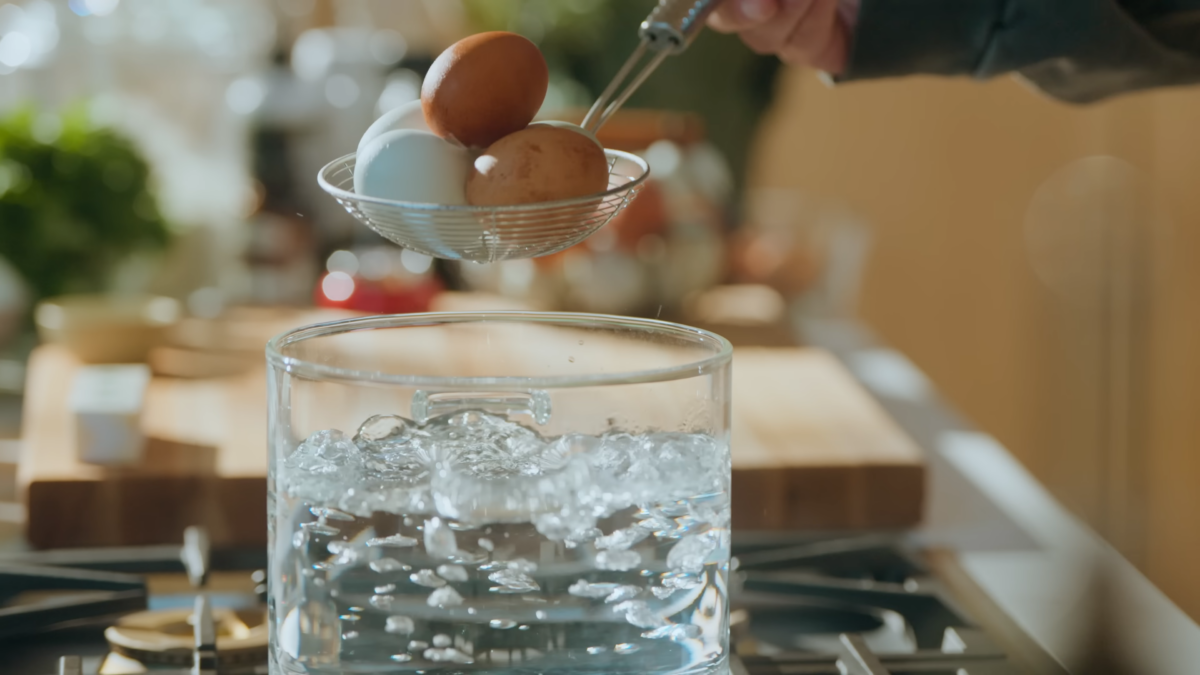 A man getting ready to place eggs in a glass pot of boiling water.