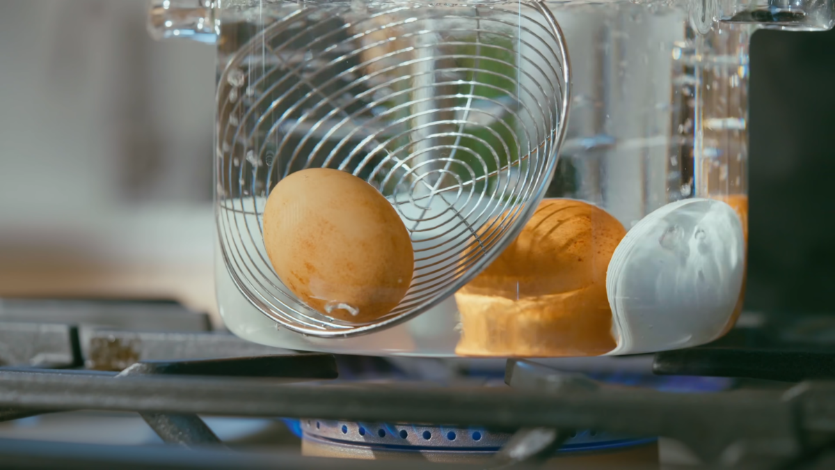 Eggs submerged in a glass pot of boiling water.