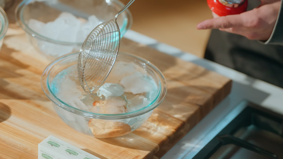 Eggs being submerged in a glass bowl of ice water.