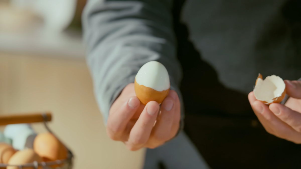A man holding a half peeled hard boiled egg.