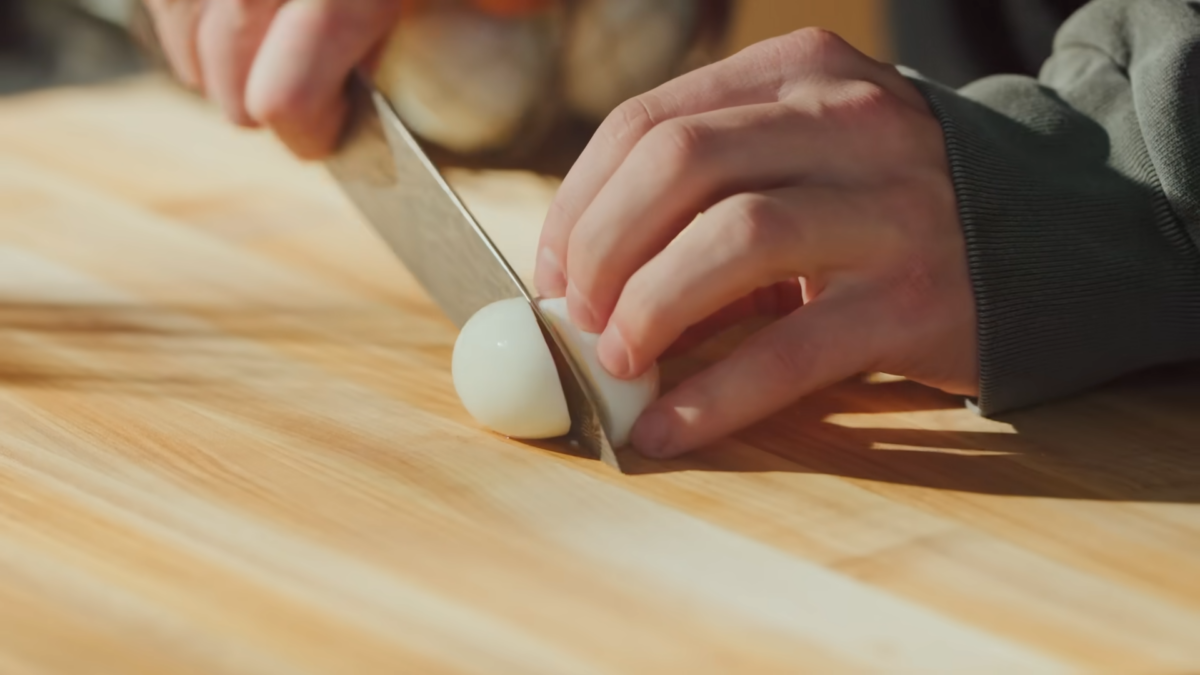 A male chef slicing a hard boiled egg on a wooden cutting board.