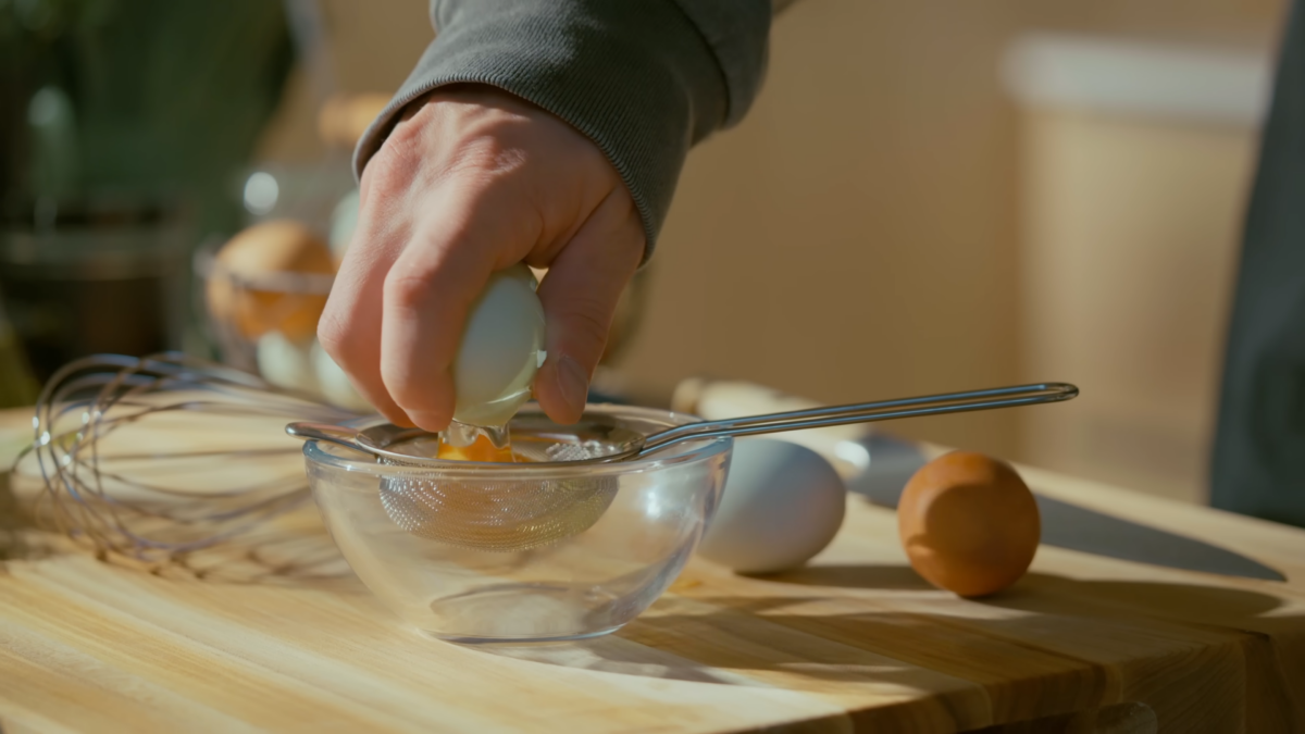 A cracked egg being strained in a sieve.