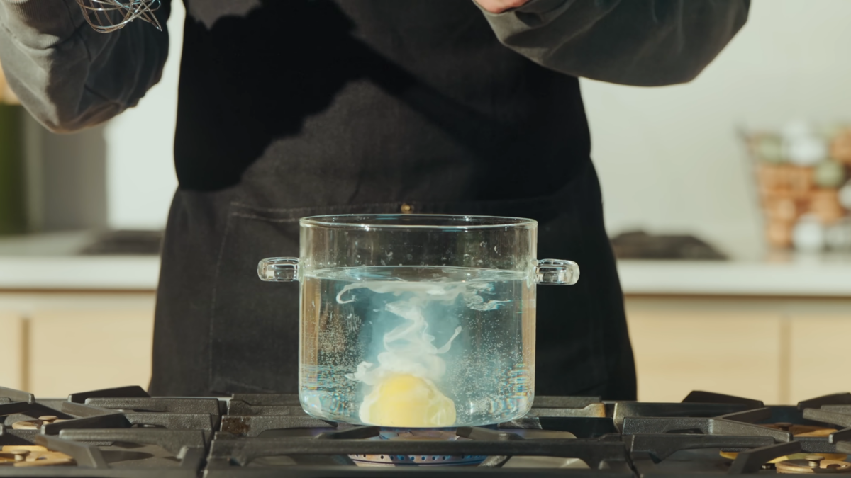 An egg in a glass pot of boiling water on a stove.