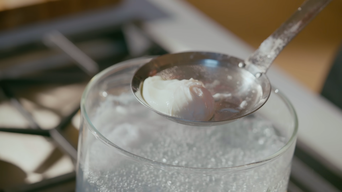 A poached egg on a slotted spoon over a pot of boiling water.