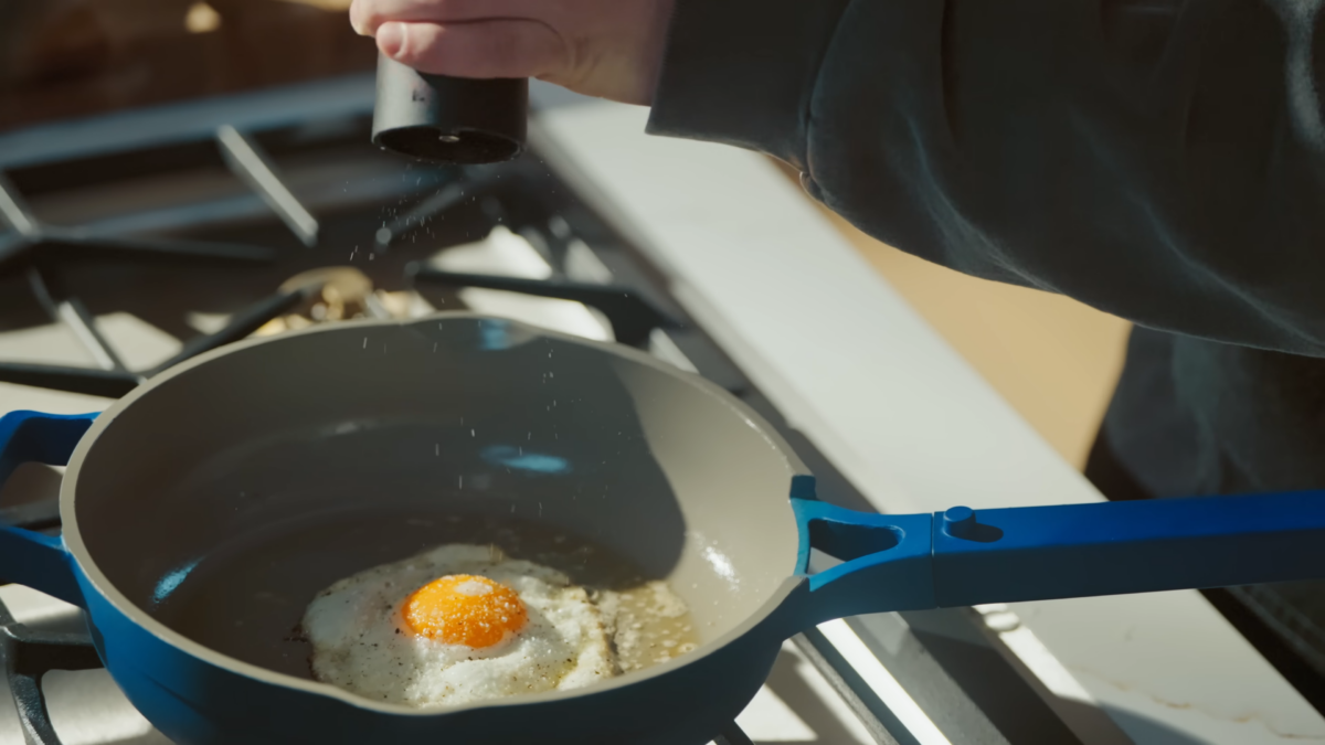 A man grinding pepper over top of an egg cooking in a skillet.