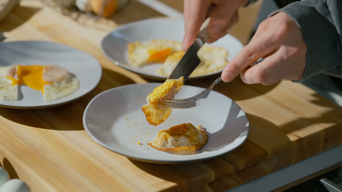 Half an over hard egg being held above a plate.