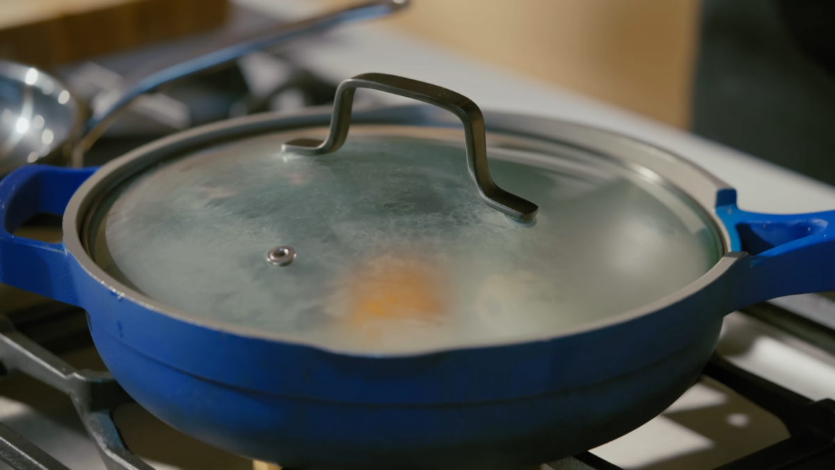 An egg cooking in a blue pan with a glass lid.