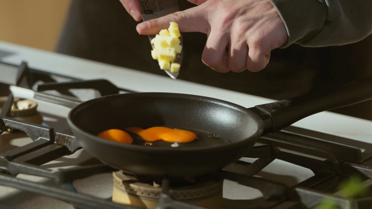 Cubed butter being tossed into a pan of raw eggs.