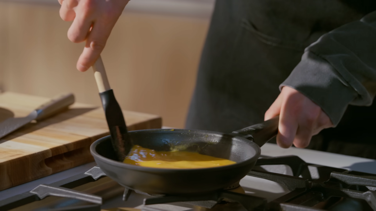 A chef mixing a pan of eggs with a rubber spatula.