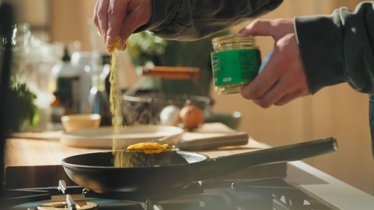 A man sprinkling seasoning into a pan of eggs.
