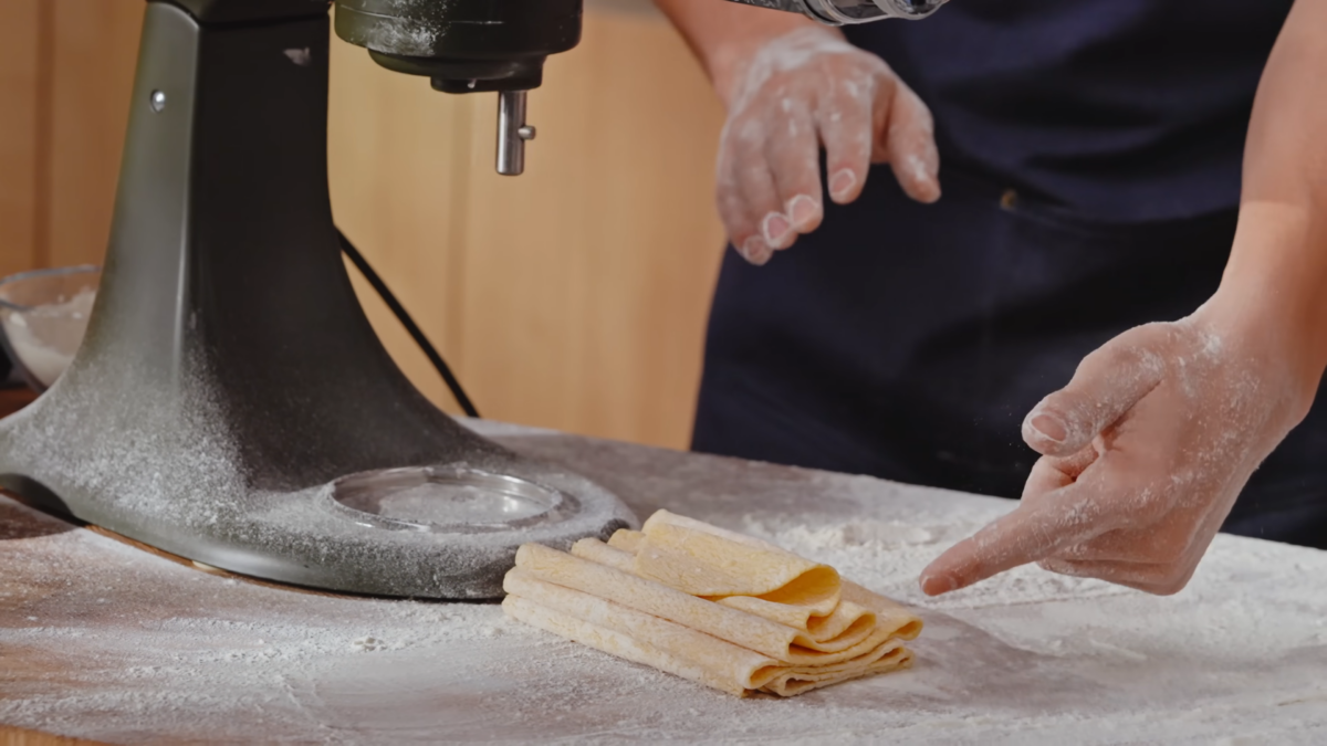 A sheet of dough folded on a cutting board covered in flour.
