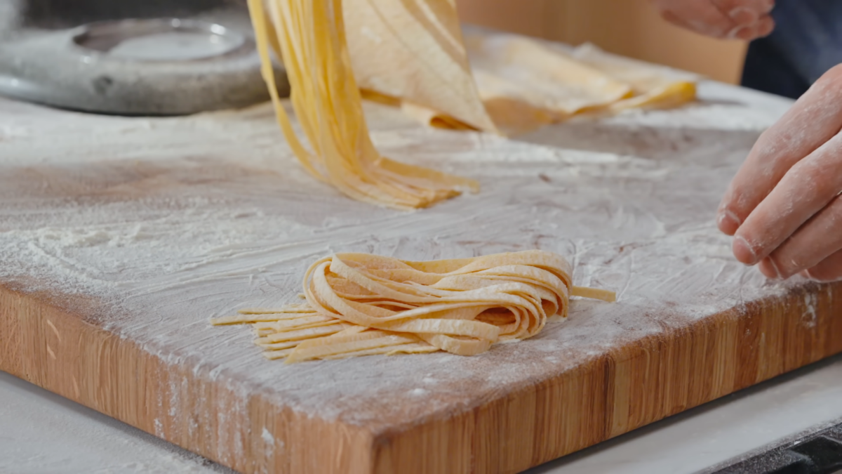 Raw fettuccine noodles on a cutting board covered in flour.