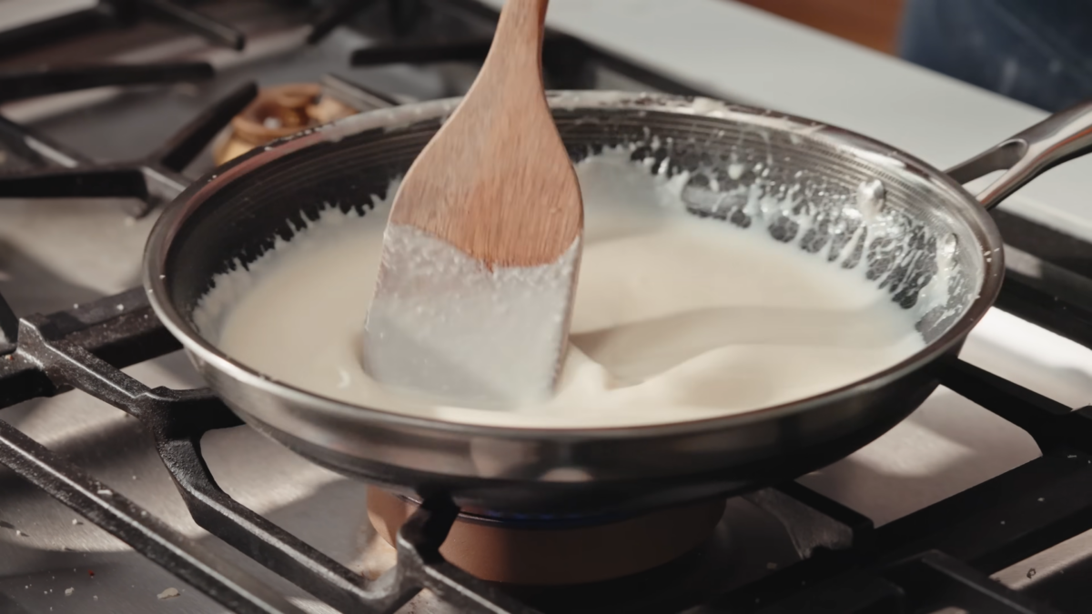 A cheesy cream sauce being mixed in a pan with a wooden spoon.