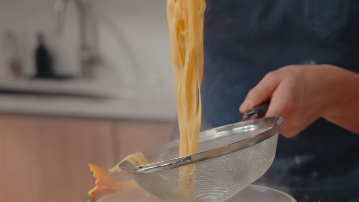 A man straining cooked fettuccine noodles.