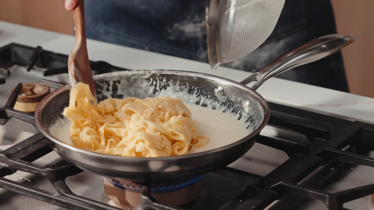 Fettuccine noodles added to a pan of creamy cheese sauce.