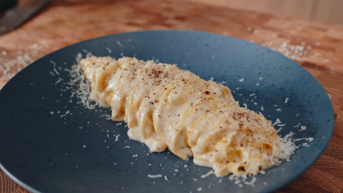 A plate fettuccine alfredo topped with fresh grated parmesan cheese and black pepper.