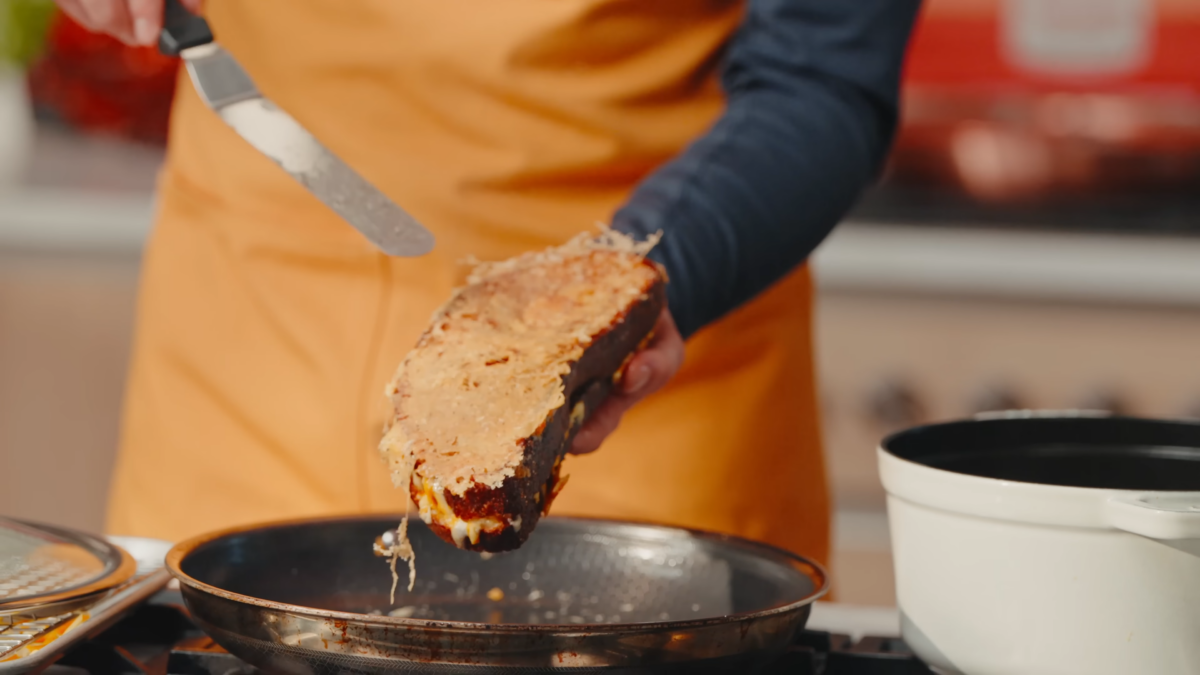 A male chef holding a grilled cheese sandwich with a parmesan crust.
