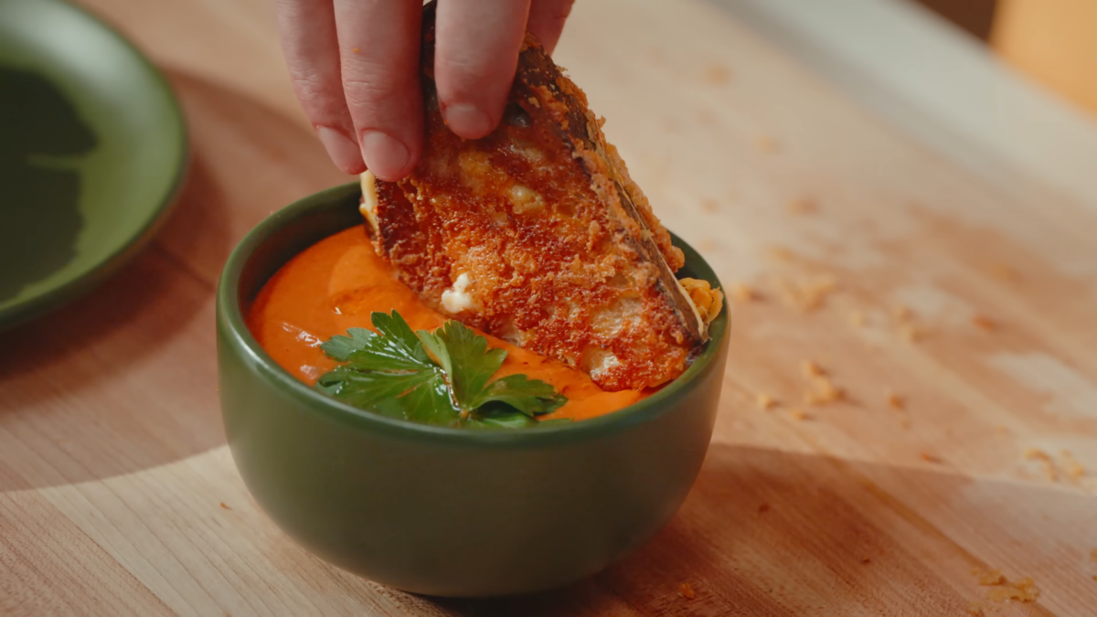 A grilled cheese sandwich dipped in a bowl of tomato soup.